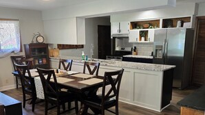 Una cocina moderna con armarios blancos, una isla central y un comedor con sillas y mesa de madera.