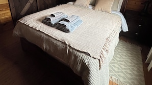 Une chambre à coucher de style cabane en bois, avec un lit, un ventilateur de plafond et une grande fenêtre avec des rideaux.