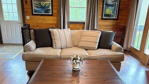 Un salon au parquet en bois, avec un canapé d’angle beige, une table basse en bois et un tapis en peau de vache noire.