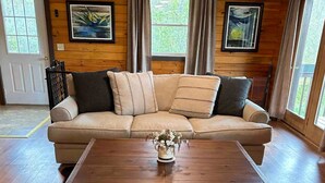 Un intérieur en bois avec un canapé beige, une table basse en bois et des œuvres d’art encadrées accrochées aux murs.