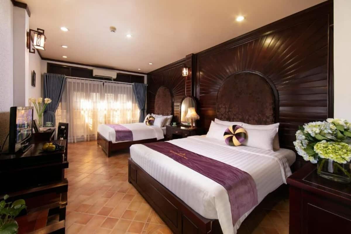 A hotel room with two beds, a TV, a desk, and a large mirror.