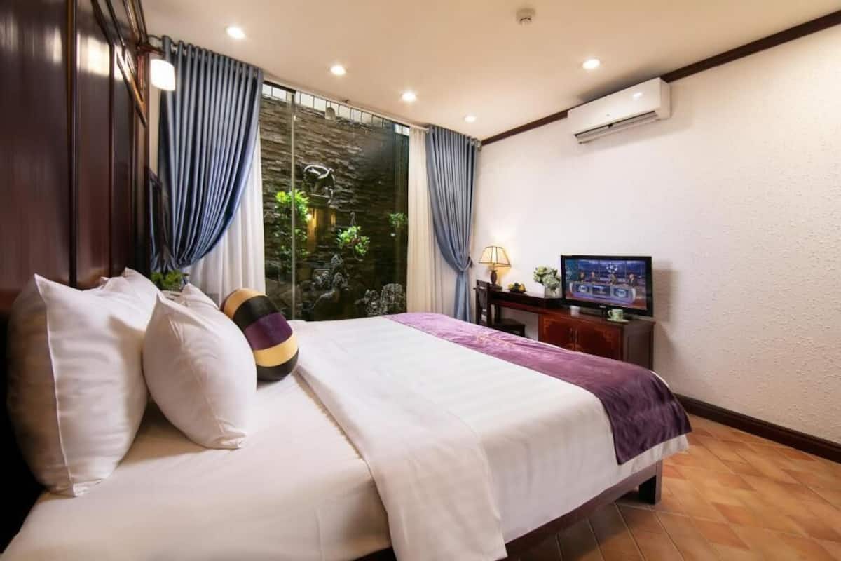 A hotel room with a bed, a TV, a desk, and a window with curtains.