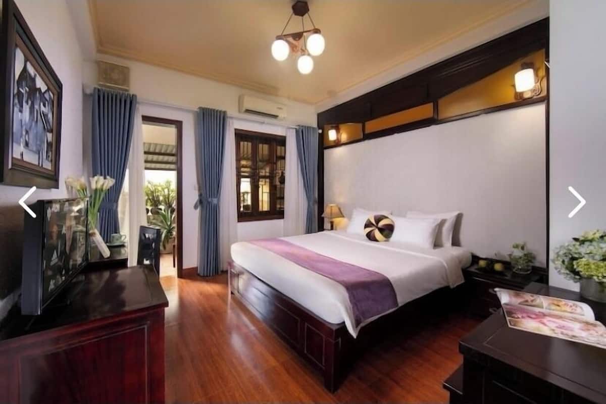 A hotel room with a large bed, a wooden headboard, a nightstand, a desk, and a window with curtains.