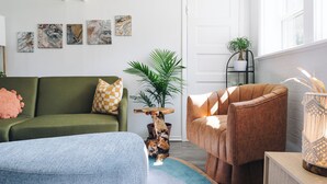 A modern living room with a green sofa, a brown armchair, and a blue ottoman. There are abstract paintings on the wall and a potted plant. - Sacramento - Stylish 2BR Apt in Irving Park (Chicago)