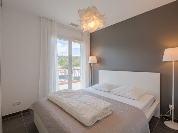 A modern bedroom with a large bed, a balcony view, and a unique ceiling light fixture.