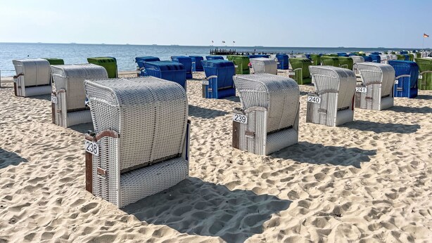 Des chaises de plage en osier, portant les numéros 218, 239, 220, 240 et 3, sont disposées sur une plage de sable, avec la mer en arrière-plan.