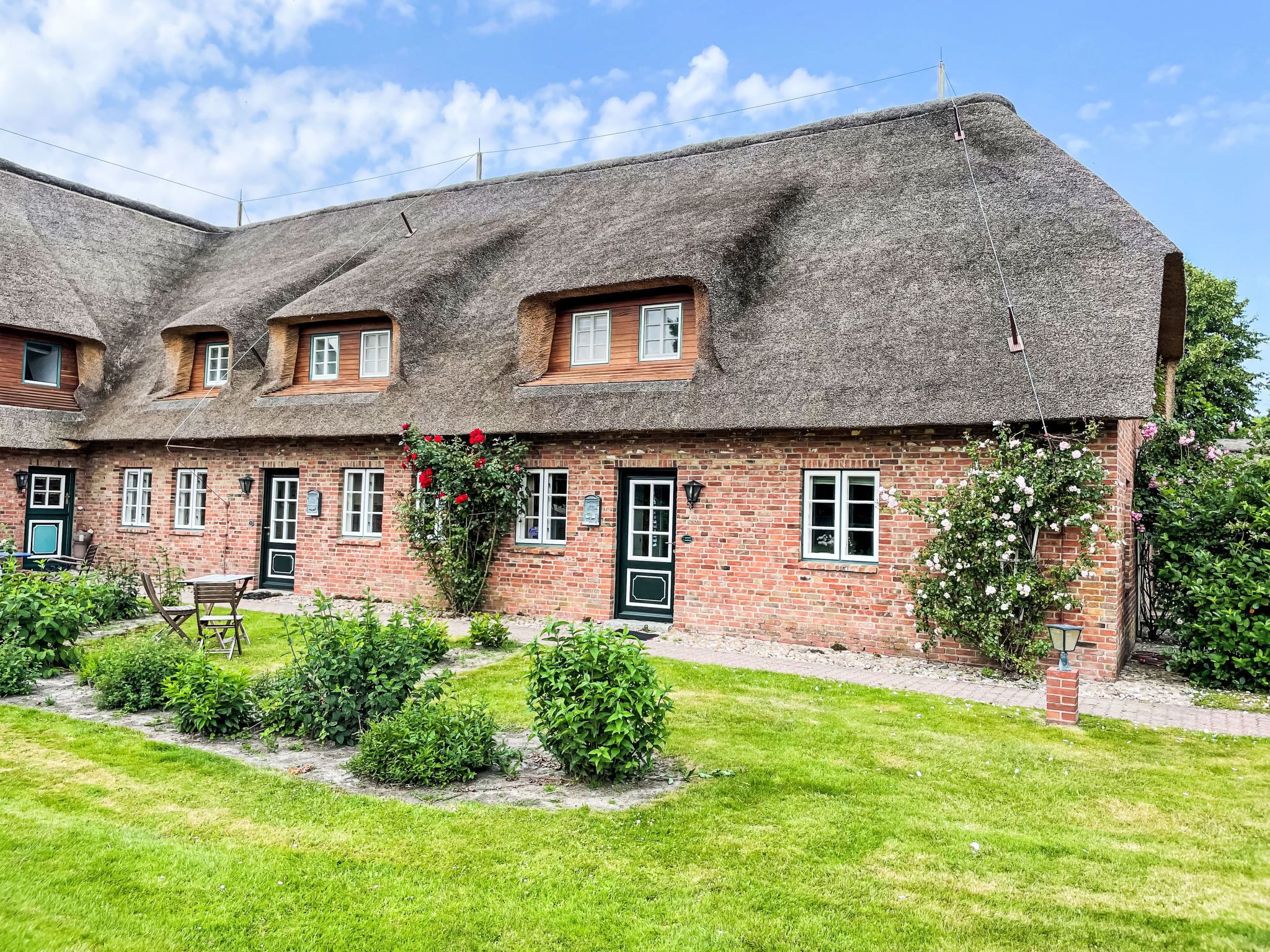Un bâtiment traditionnel en briques, doté d’un toit de chaume, de nombreuses fenêtres et d’un petit jardin agrémenté de verdure et de fleurs.