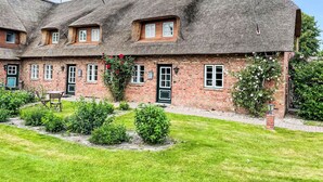 Un bâtiment traditionnel en briques, doté d’un toit de chaume, de nombreuses fenêtres et d’un petit jardin agrémenté de verdure et de fleurs.
