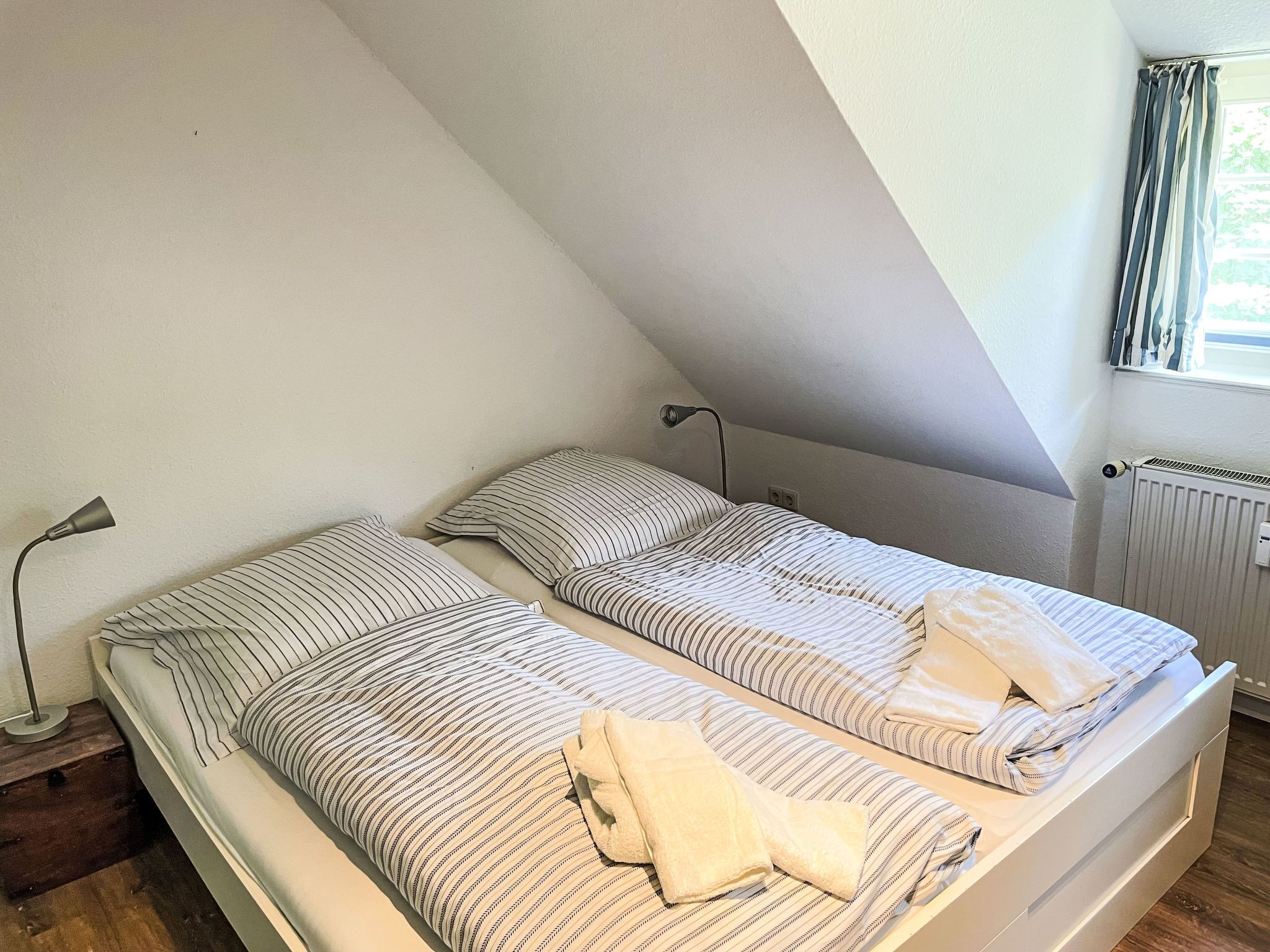 Ein kleines Zimmer mit Einzelbetten, Heizkörper und einem Vorhangfenster.
