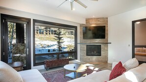 A modern living room with a fireplace, large windows, and a cozy seating area. - Walk to Skiing, Exceptional Juniper Landing 5 BR, Private Hot Tub, Golf Course Views, Outdoor Pool (Park City)