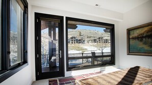 A bedroom with a large window, a view of a building complex, and a painting on the wall. - Walk to Skiing, Exceptional Juniper Landing 5 BR, Private Hot Tub, Golf Course Views, Outdoor Pool (Park City)