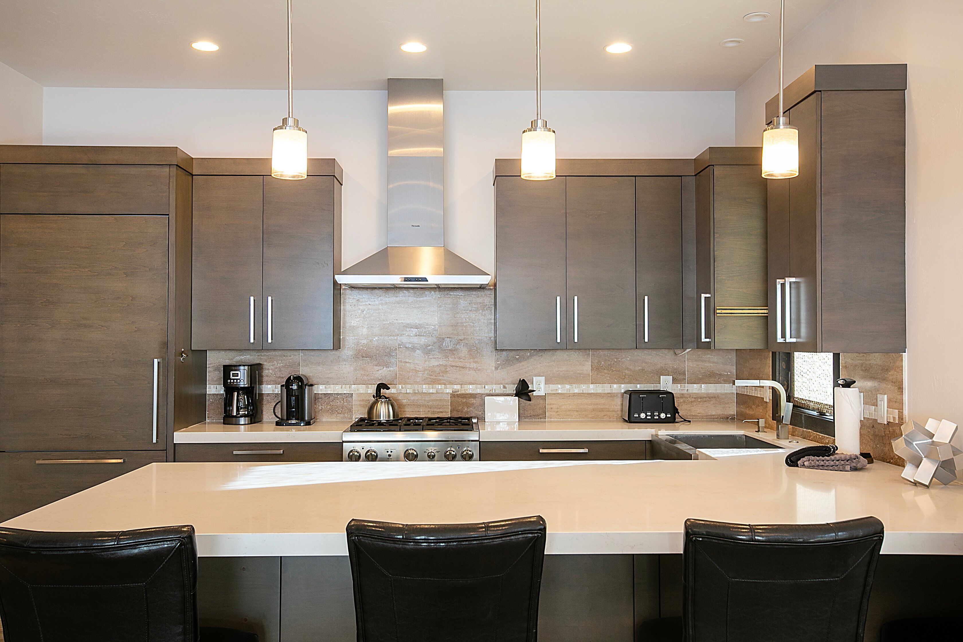 A modern kitchen with dark wood cabinets, a central island with bar stools, stainless steel appliances, and pendant lighting.