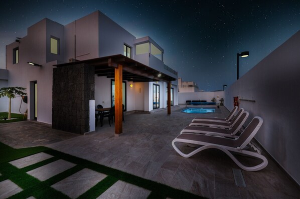 A modern outdoor pool area with lounge chairs, a stone pillar, and a clear night sky.