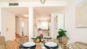 A dining area with a glass table, wicker chairs, and a view into the kitchen.