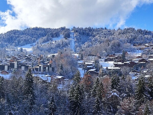 Un village de montagne enneigé, avec ses maisons traditionnelles en bois, un télésiège et un ciel dégagé.