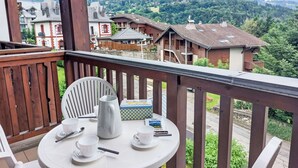 A balcony with a table set for tea, overlooking a mountainous village with traditional houses. - Cosy apartment for 4 people with WIFI, TV and balcony (Saint-gervais-les-bains)