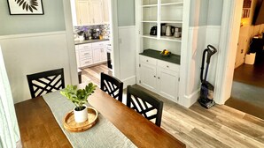 A dining area with a wooden table, chairs, and a potted plant. There is a kitchen in the background with white cabinets and a tiled backsplash. - Crosby Street Suite - Freshly Renovated 3 Bedroom near Downtown Augusta (Augusta)