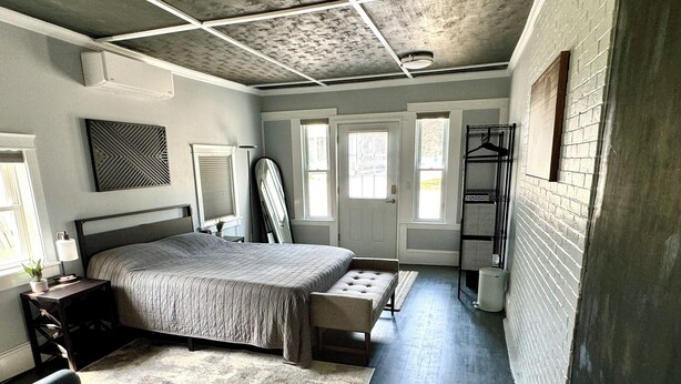 A bedroom with a large bed, a desk, a chair, a bench, a wardrobe, and a radiator. - Crosby Street Suite - Freshly Renovated 3 Bedroom near Downtown Augusta (Augusta)