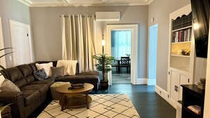 A living room with a brown leather sofa, a round coffee table, a patterned rug, a potted plant, and a bookshelf. - Crosby Street Suite - Freshly Renovated 3 Bedroom near Downtown Augusta (Augusta)