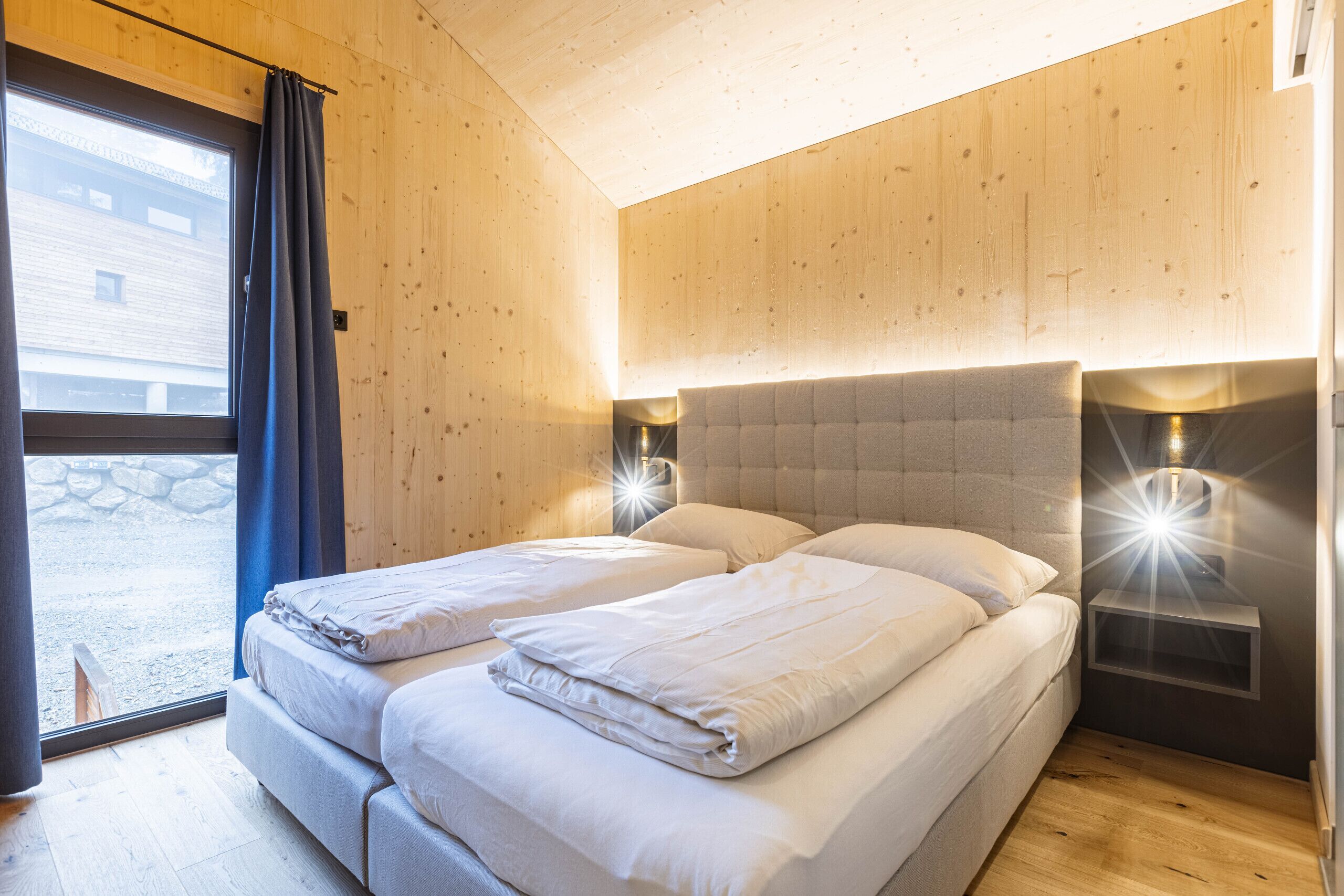A double bed with two pillows, a nightstand with a lamp, and a window with curtains.