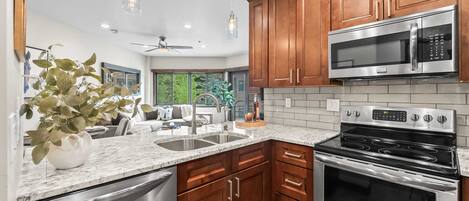 A modern kitchen with wooden cabinets, stainless steel appliances, and a marble countertop.
