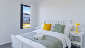 Een keurig opgemaakte slaapkamer met een bed, kussens, een nachtkastje en een raam.