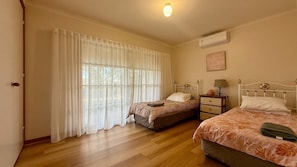 Une chambre avec deux lits, une fenêtre avec des rideaux légers, une table de chevet avec une lampe et un appareil de climatisation fixé au mur.