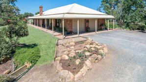 A house with a covered porch, brick exterior, and a well-maintained garden with rocks and plants.