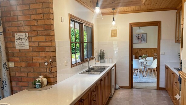 A kitchen with a brick wall, wooden ceiling, and a view into a dining area.