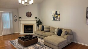A living room with a fireplace, a sofa, a coffee table, and a chandelier. - Cozy home with AC and WiFi in beautiful Flowery Branch (Flowery Branch)