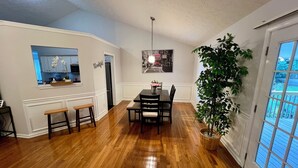 A dining area with a wooden table and chairs, a bench, a potted plant, and a kitchen visible through an open door. - Cozy home with AC and WiFi in beautiful Flowery Branch (Flowery Branch)
