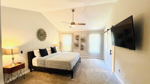 A bedroom with a bed, a desk, a lamp, a ceiling fan, and a TV mounted on the wall. - Cozy home with AC and WiFi in beautiful Flowery Branch (Flowery Branch)
