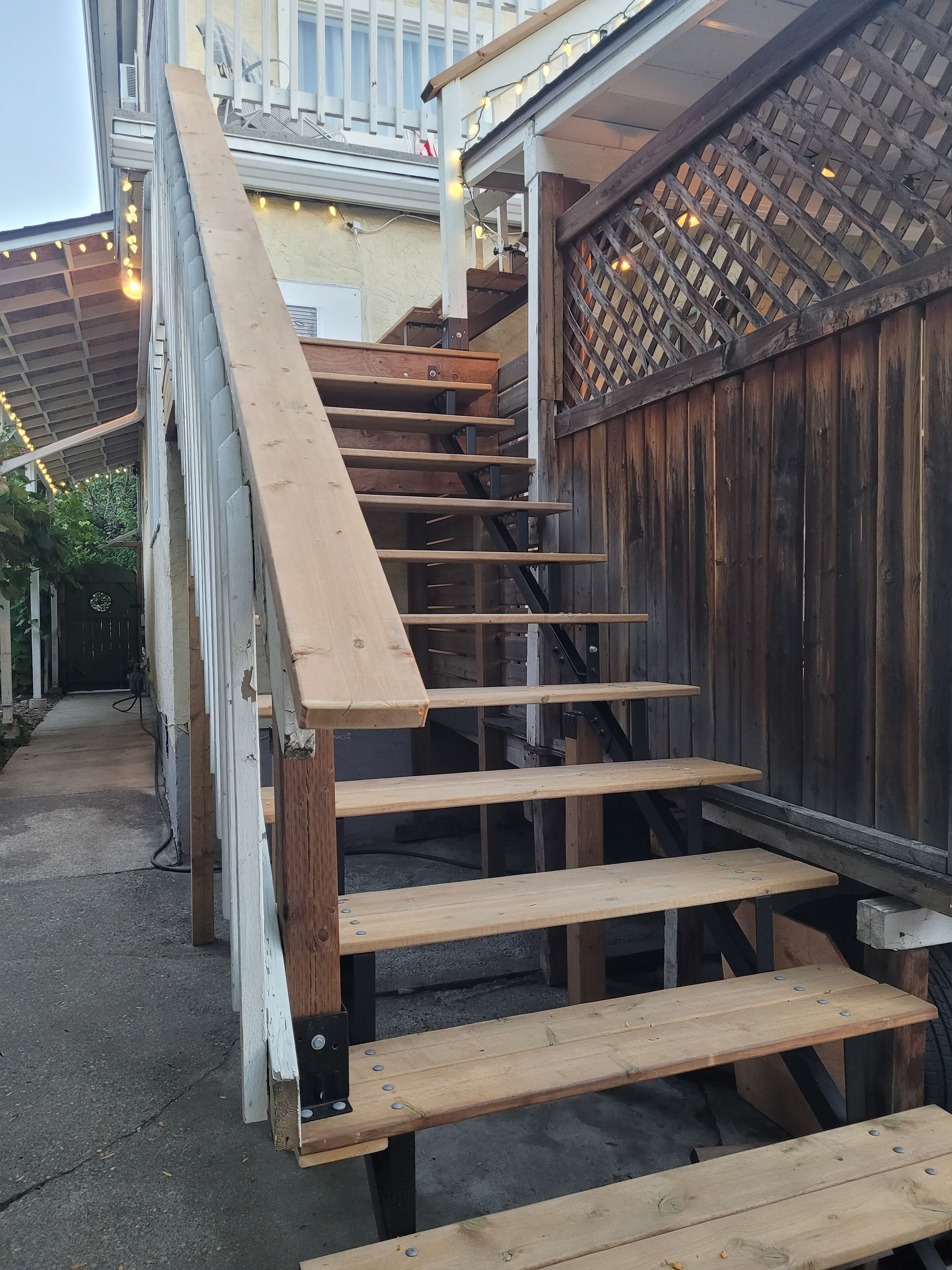 Un escalier en bois avec des rampes métalliques menant à un espace extérieur abrité.