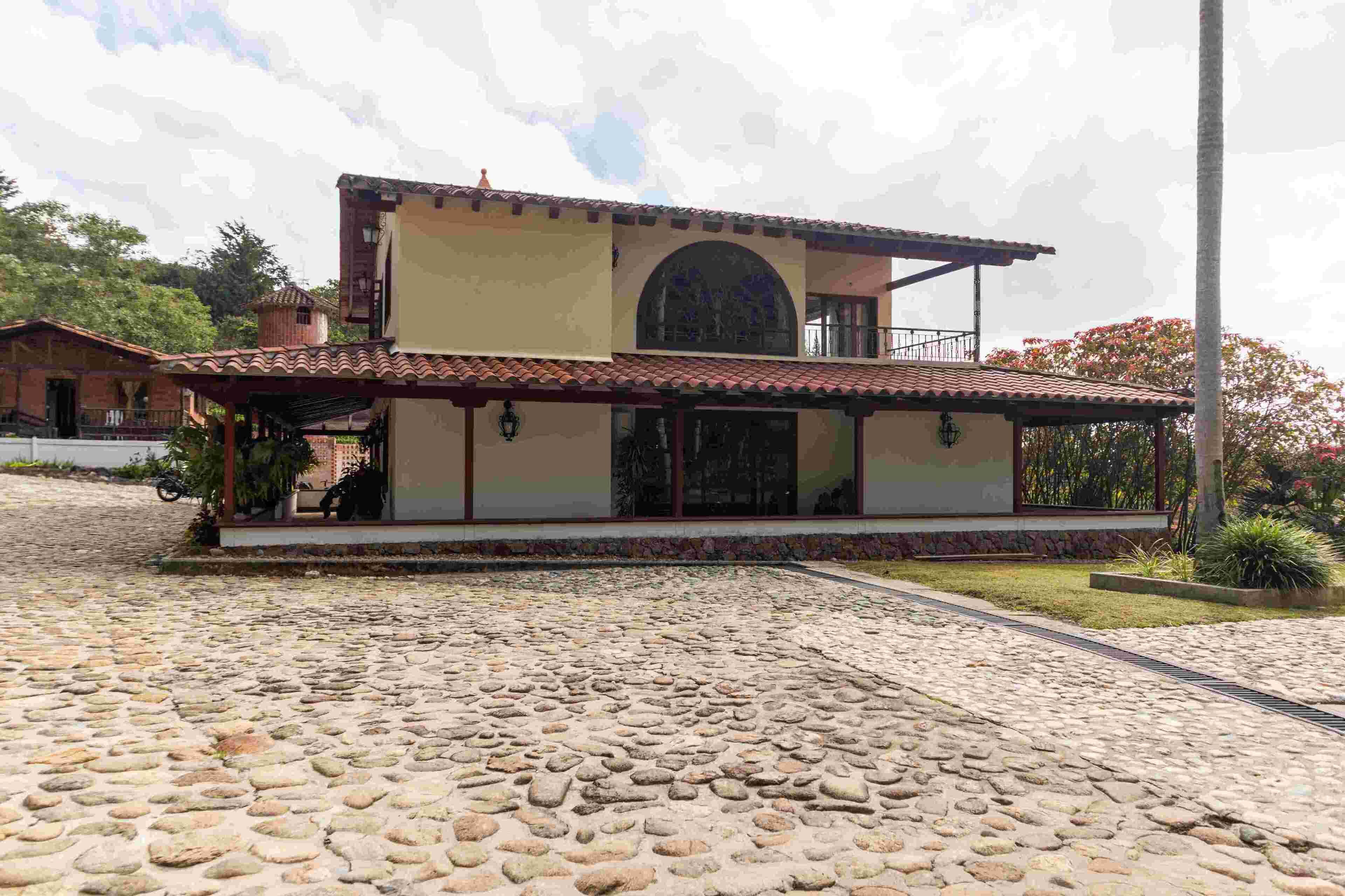 Un edificio de dos pisos con techo de tejas, un balcón y un patio empedrado con piedra.