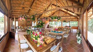 A spacious indoor venue with high ceilings and natural light, featuring wooden tables and chairs, and various floral arrangements.