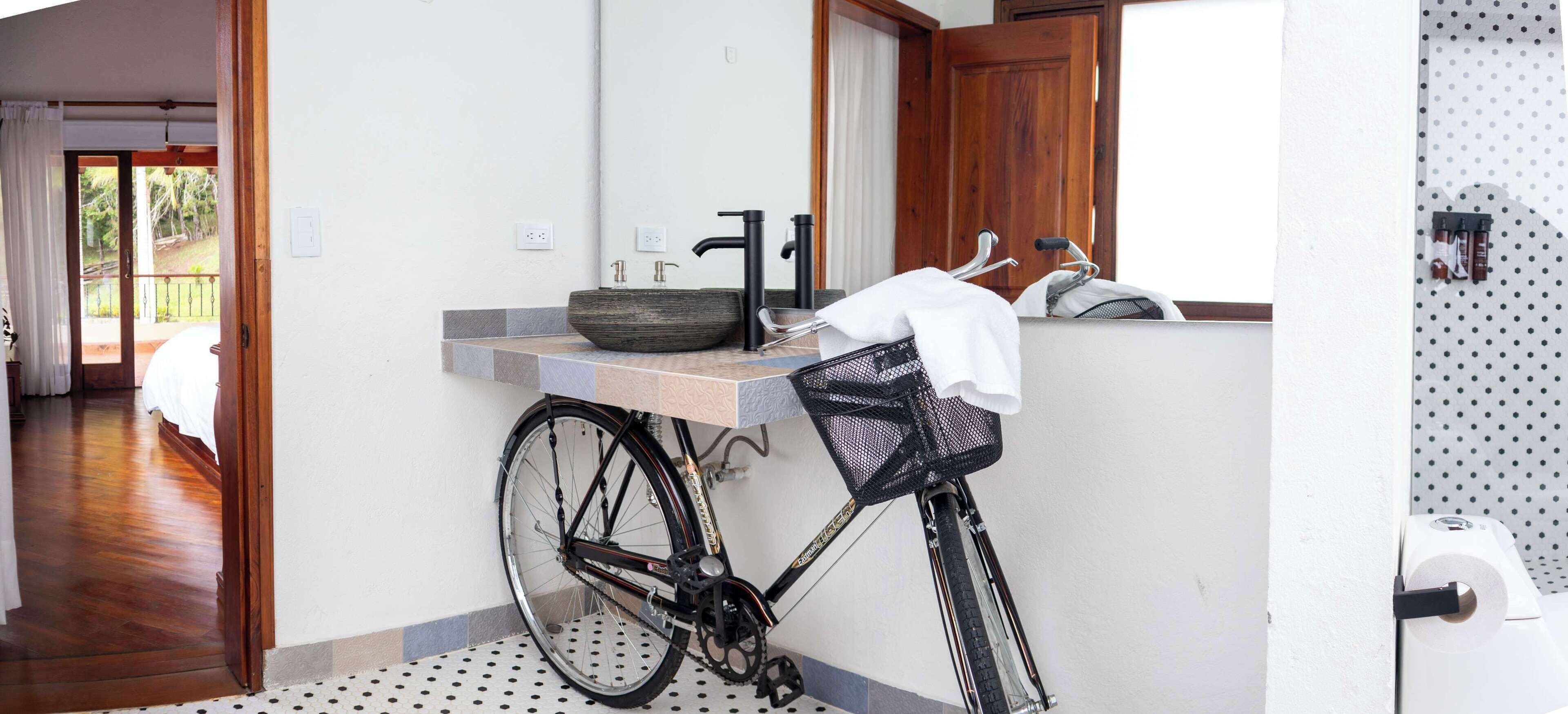 Um banheiro com janela de madeira, pia com torneira preta e uma bicicleta encostada na parede.