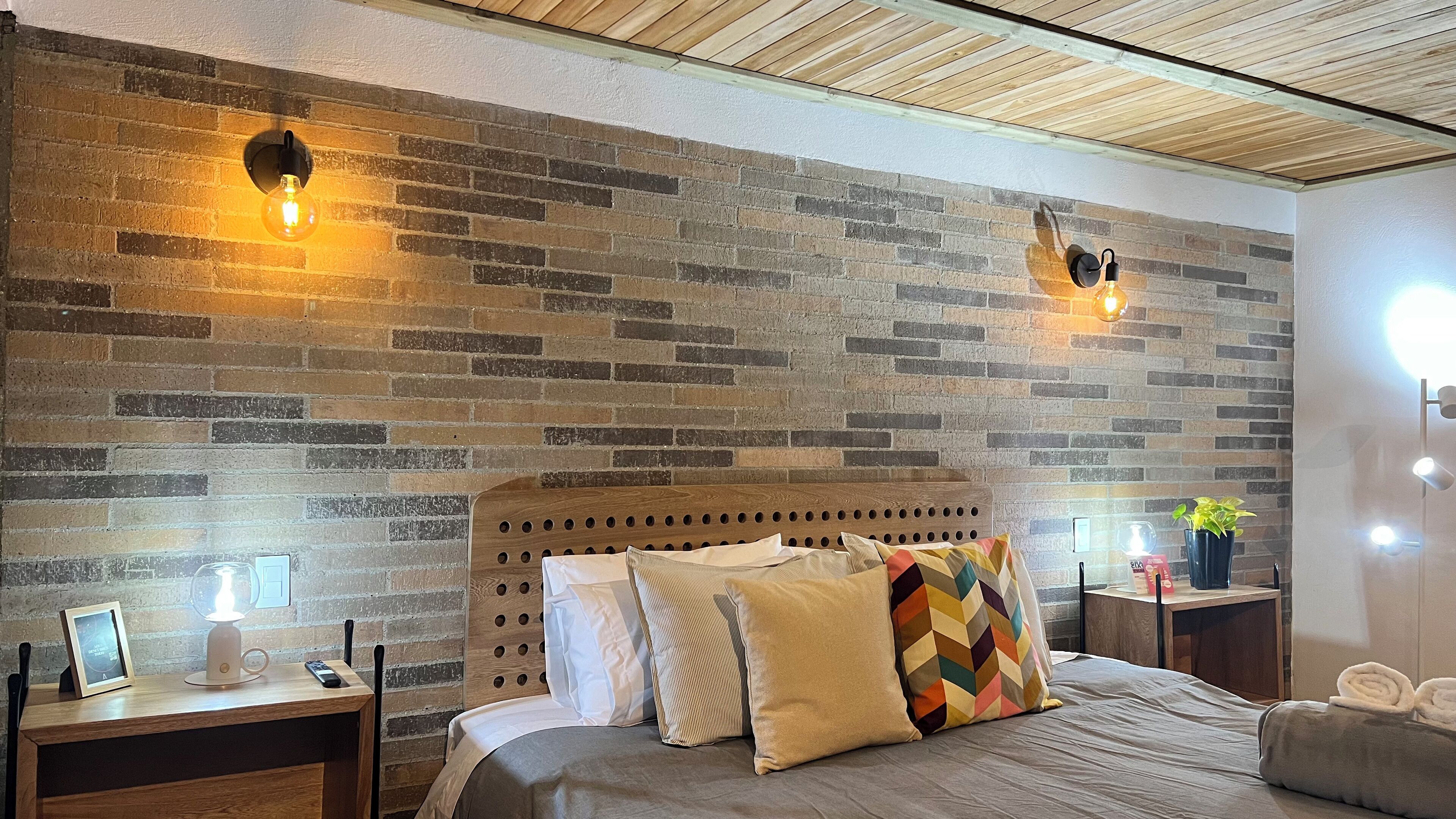 A bedroom with a brick-patterned wall, a wooden headboard, and two bedside lamps.