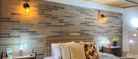 A bedroom with a brick-patterned wall, a wooden headboard, and two bedside lamps.