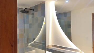 A modern bathroom with a glass shower enclosure, a curved white wall, and a tiled floor.