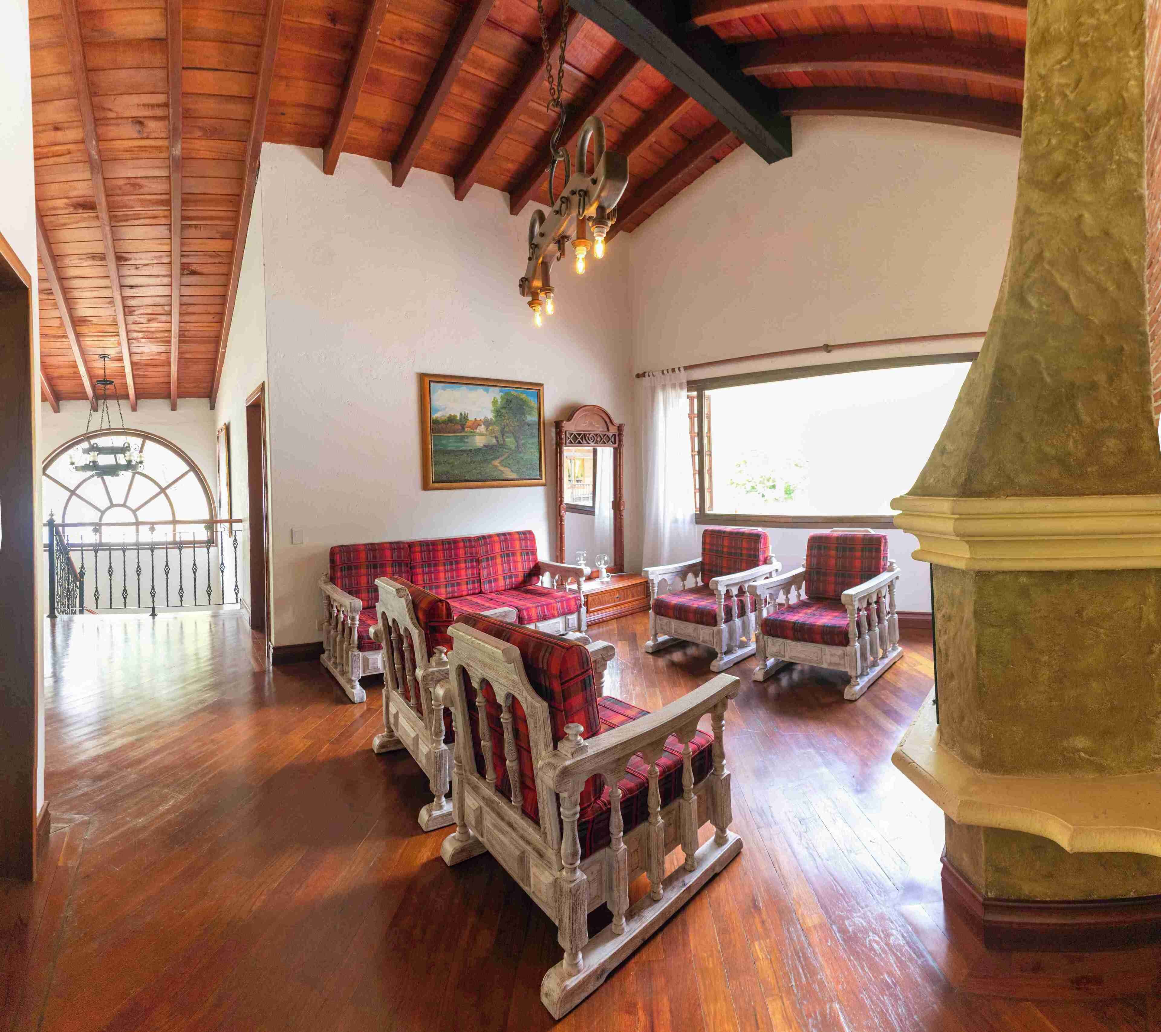 A spacious room with wooden flooring, a high ceiling, and a large window. There are several plaid-patterned chairs and a sofa.