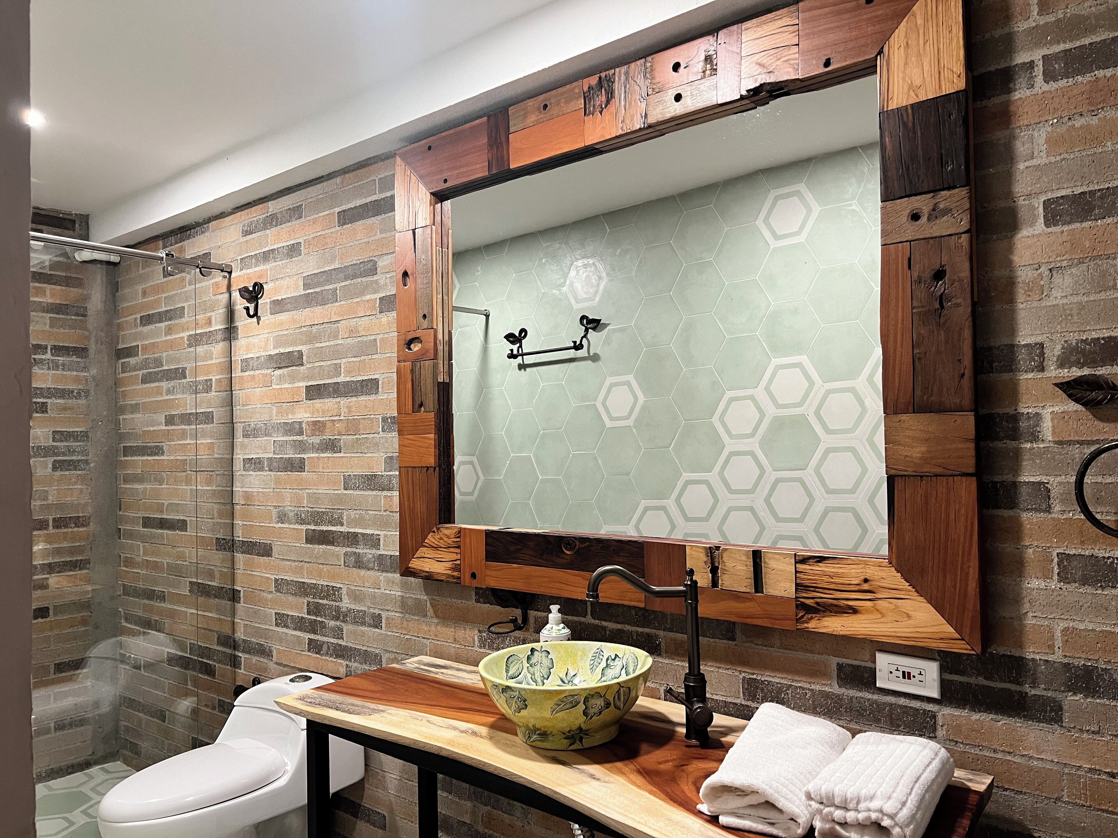 A bathroom with a wooden vanity, a green ceramic sink, and a white toilet.