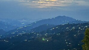Paesaggio montuoso con luci sparse che segnalano presenza di insediamenti, sotto un cielo crepuscolare con il sole che tramonta o sorge.