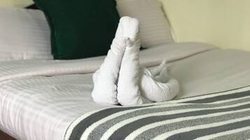 Una cama con una manta a rayas, una almohada verde y un par de toallas blancas dobladas sobre la cama.