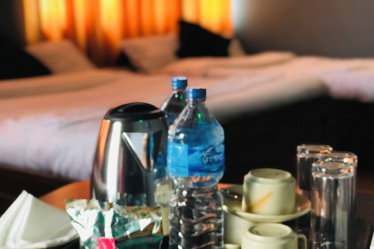 Une chambre d’hôtel avec un lit, une table de chevet sur laquelle se trouvent une bouteille d’eau, une tasse et un verre.