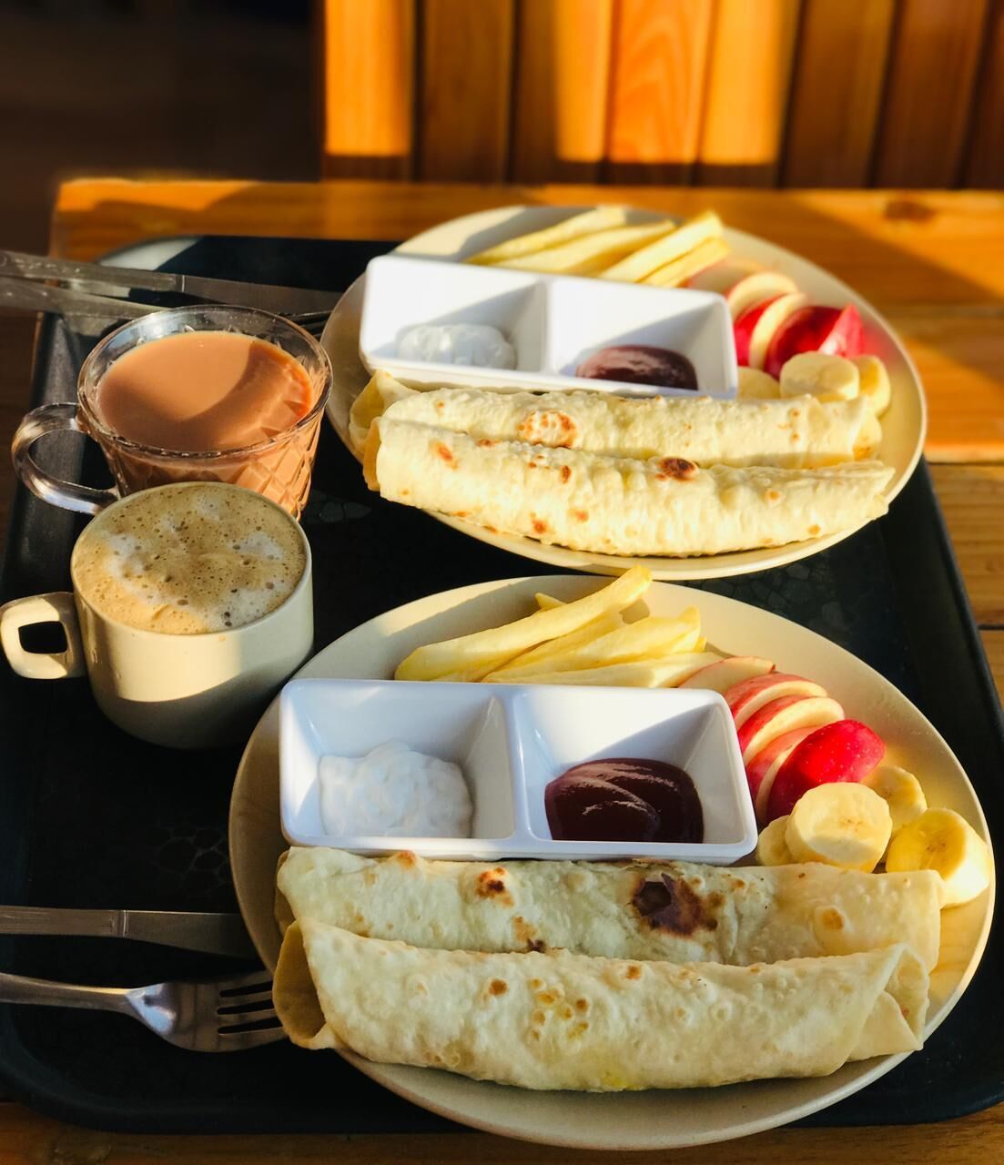 Un plateau contenant divers éléments pour le petit-déjeuner, notamment des crêpes, des fruits et du café.