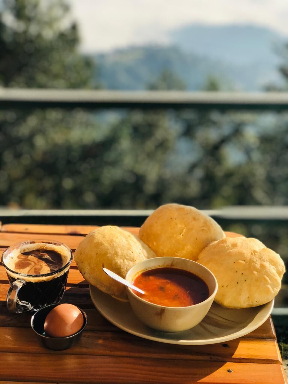 A table with a plate of bread rolls, a cup of coffee, and a bowl of sauce.