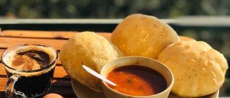 A table with a plate of bread rolls, a cup of coffee, and a bowl of sauce.