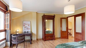 Ein Schlafzimmer mit einem Holzkapuzen, einem großen Spiegel, einem Bett mit grüner Decke und einem Fenster mit Vorhängen.