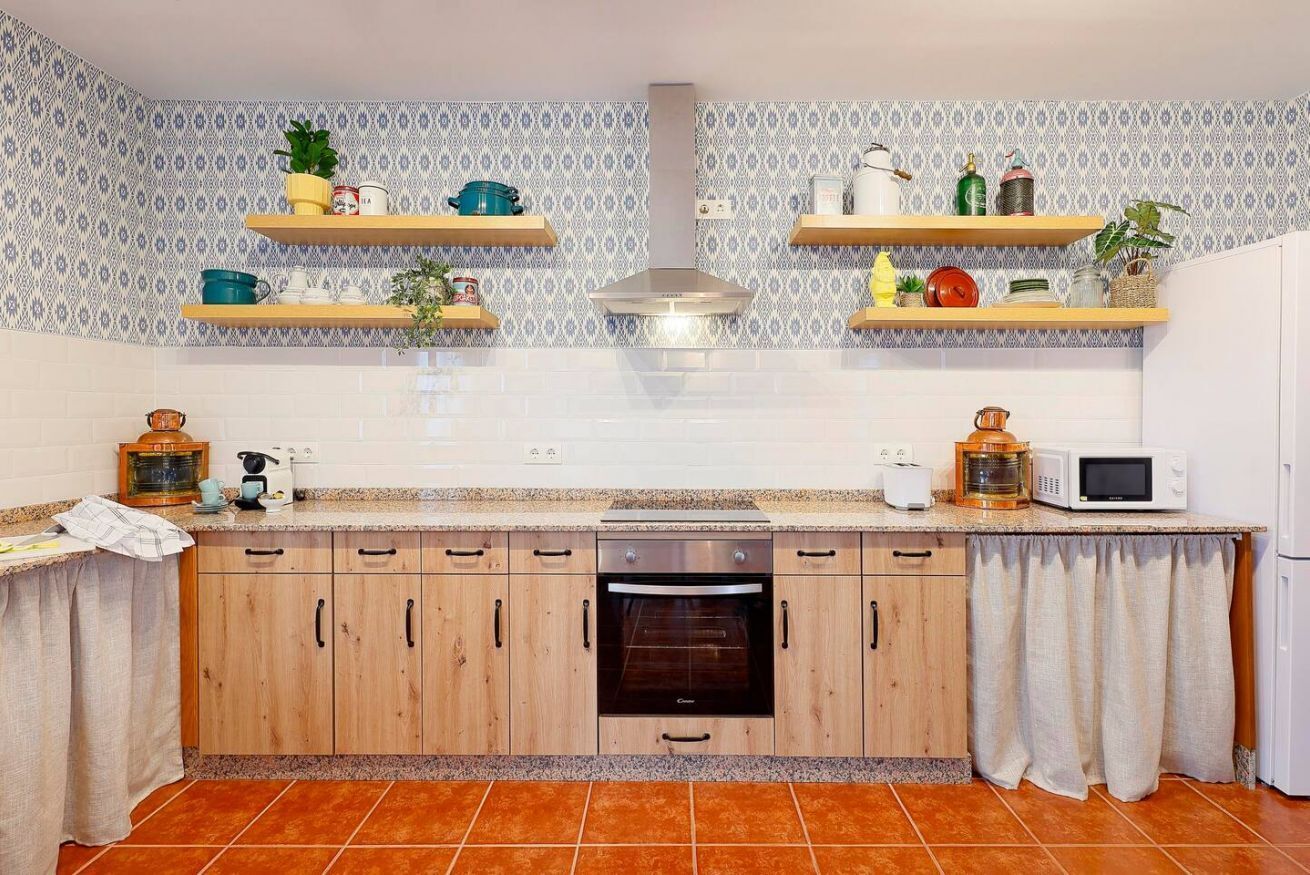Une cuisine avec des meubles de rangement en bois, un four encastré, un four à micro-ondes et divers ustensiles de cuisine rangés sur des étagères.