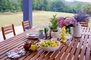 Une table en bois, dressée avec des assiettes, un saladier de fruits, une carafe, un vase de fleurs et une statuette décorative.